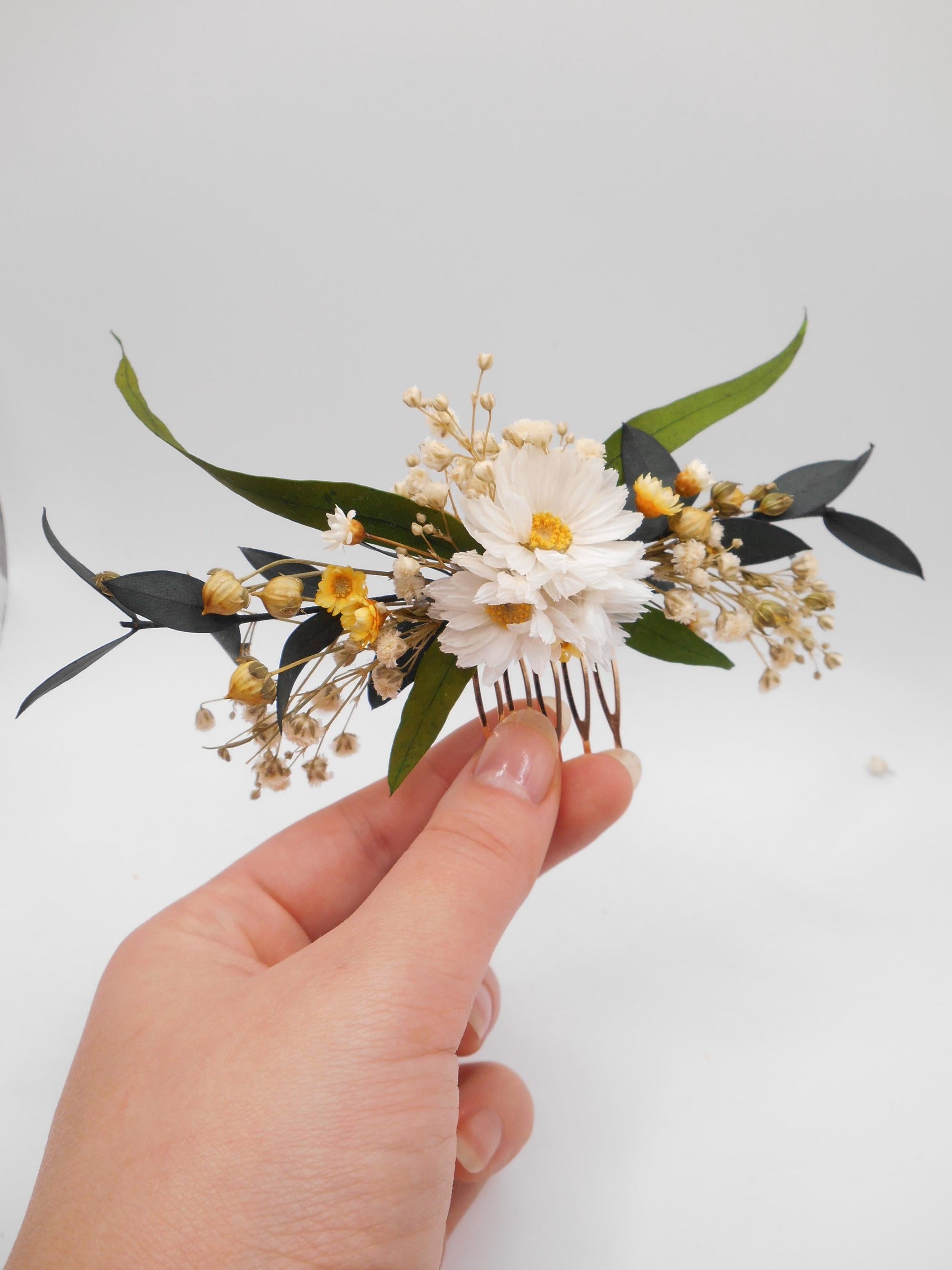 Hand holding a dried flower hair comb on a golden metal  base with daisies and green eucalyptus